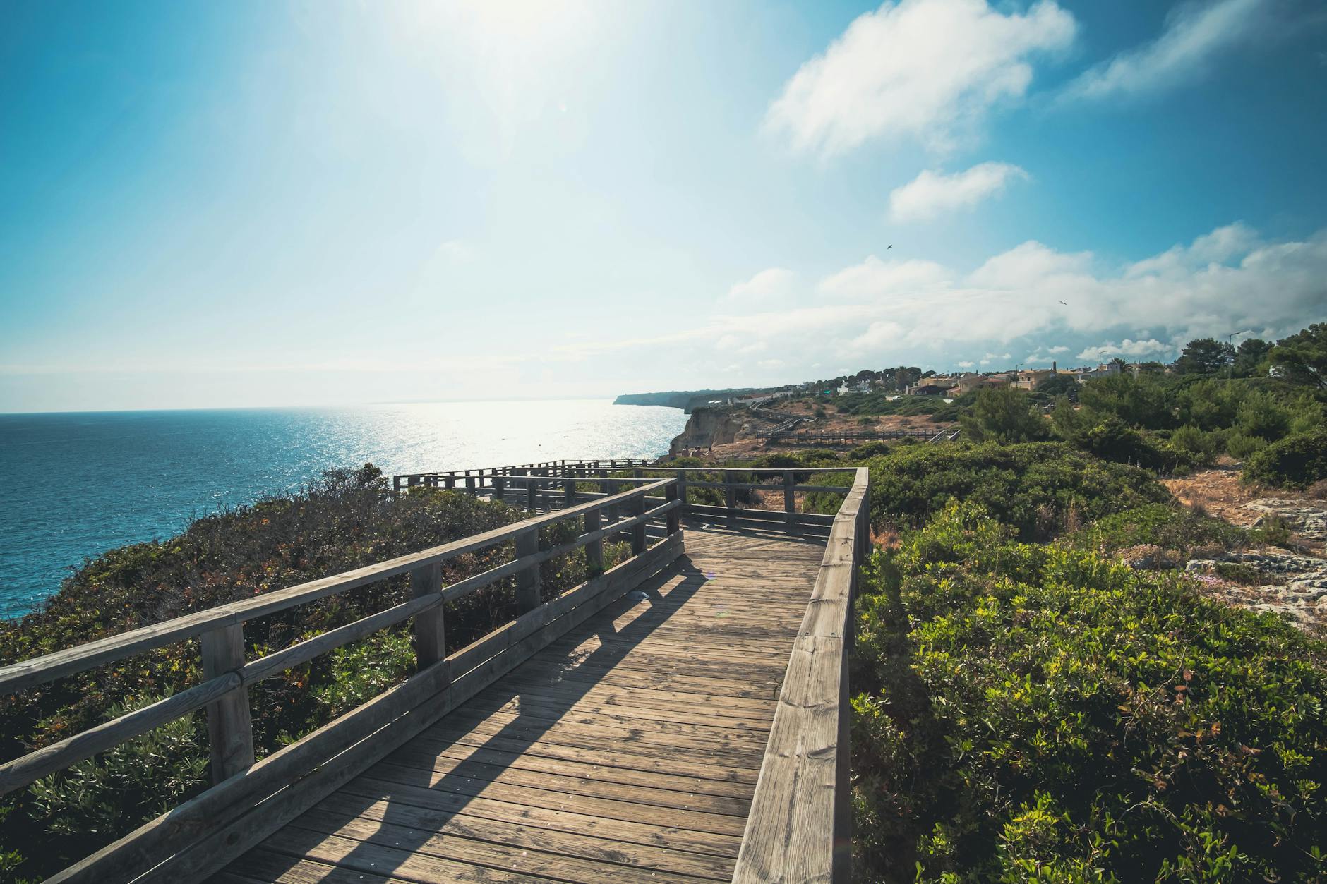 Algarve, Portugal - Ein Holzsteg führt entlang einer felsigen Küste mit Blick auf das Meer und üppige Vegetation.