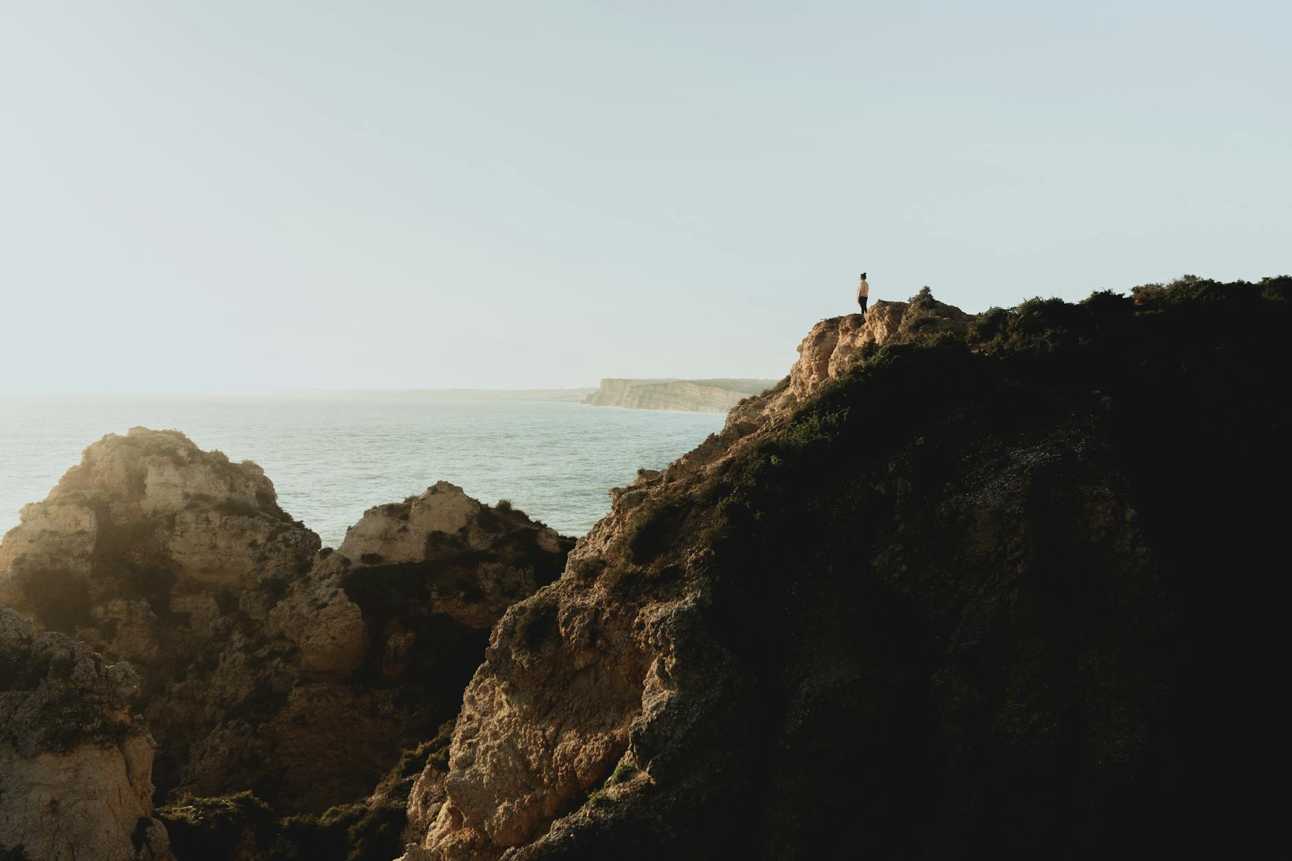 Algarve, Portugal - Eine Person steht auf einer Klippe und blickt auf das Meer.