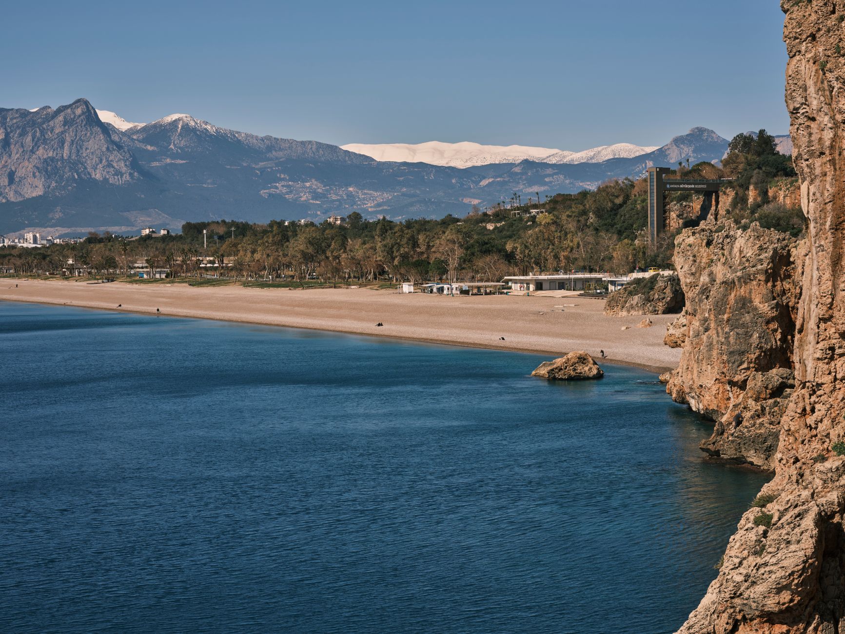 Antalya - Beautiful beach with rocky shore and mountain backdrop under a clear blue sky.