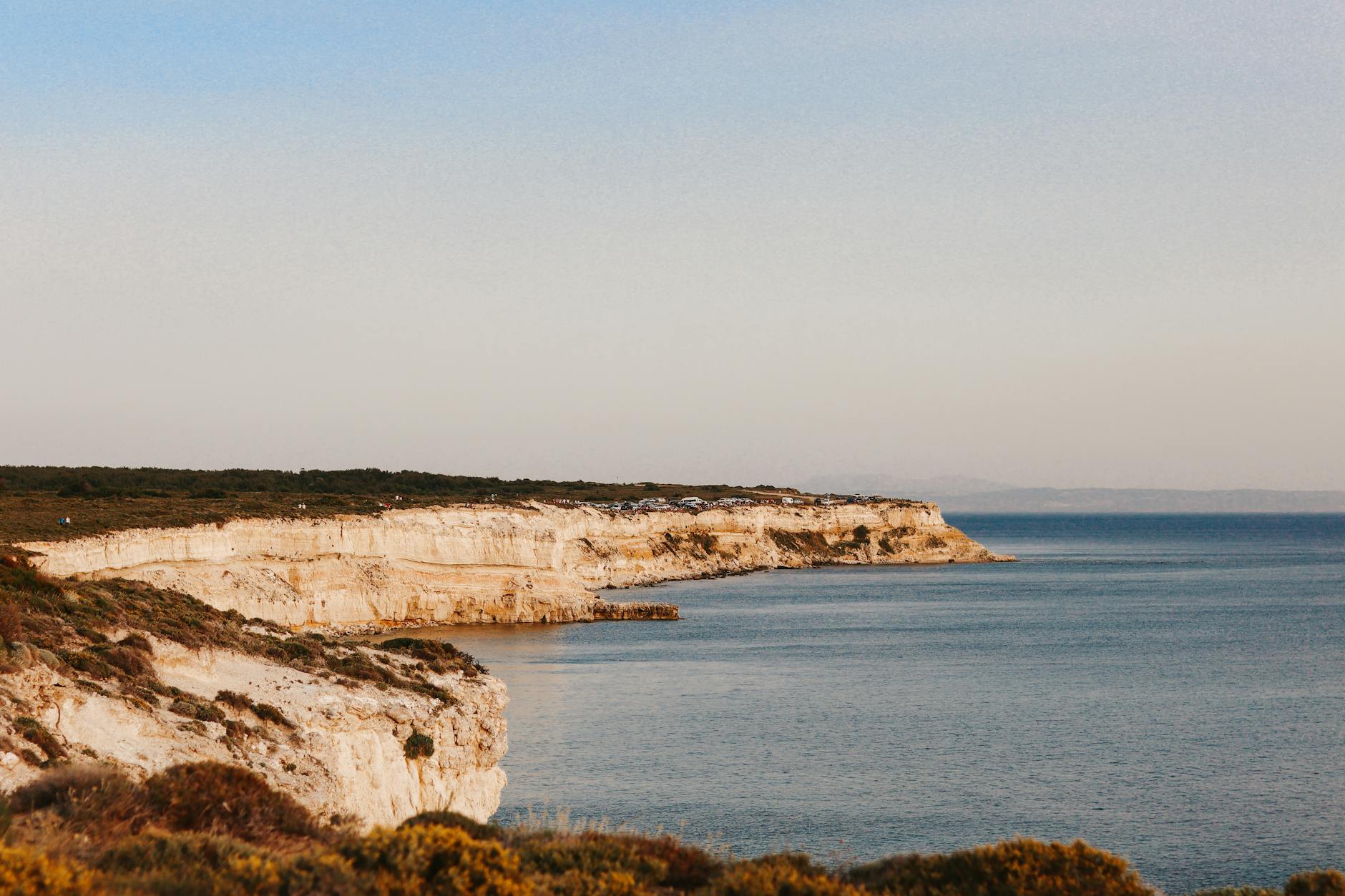Eine felsige Klippe mit Vegetation und dem Meer im Vordergrund und Hintergrund.
