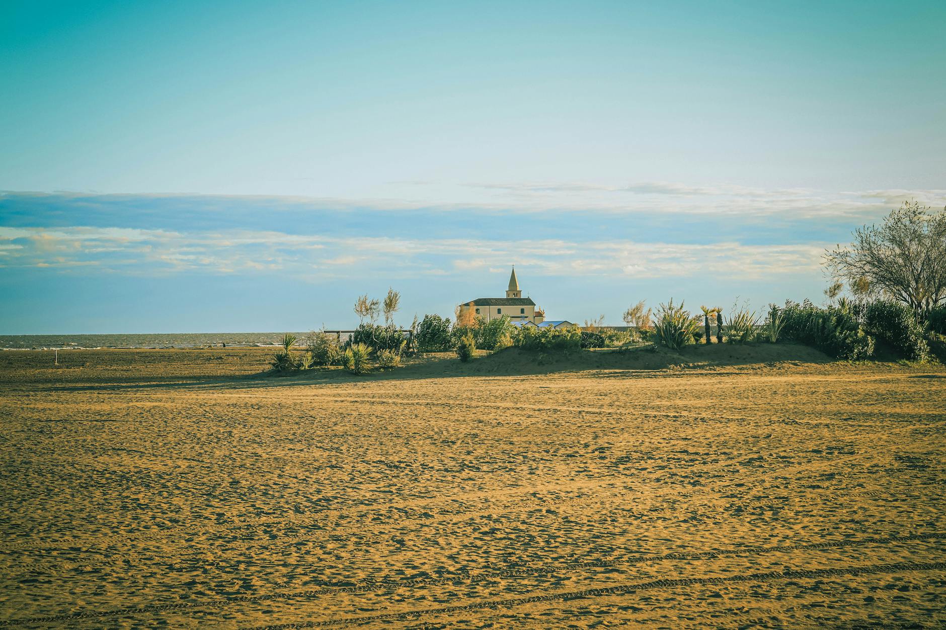 Ein Sandstrand mit einer Kirche im Hintergrund und dem Meer am Horizont.