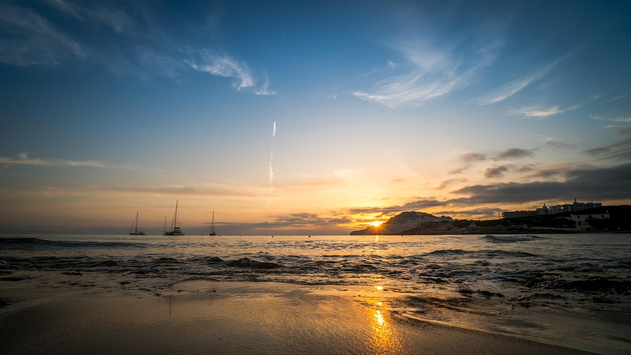 Ein Sonnenuntergang am Meer mit Booten im Wasser und einer Hotelanlage am Ufer.