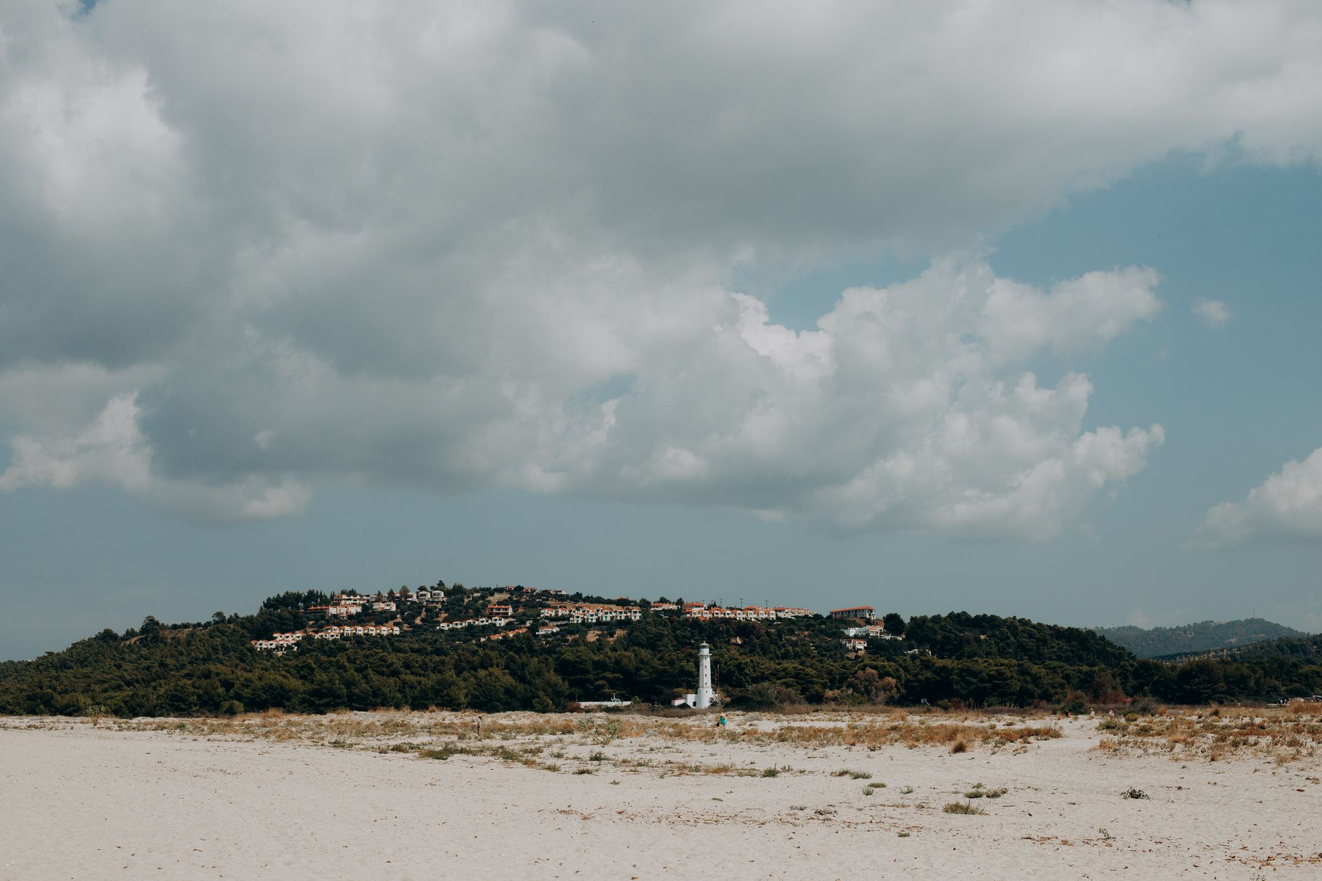 Chalkidiki, Griechenland - Scenic Greek beach landscape with lighthouse and hillside village under fluffy c