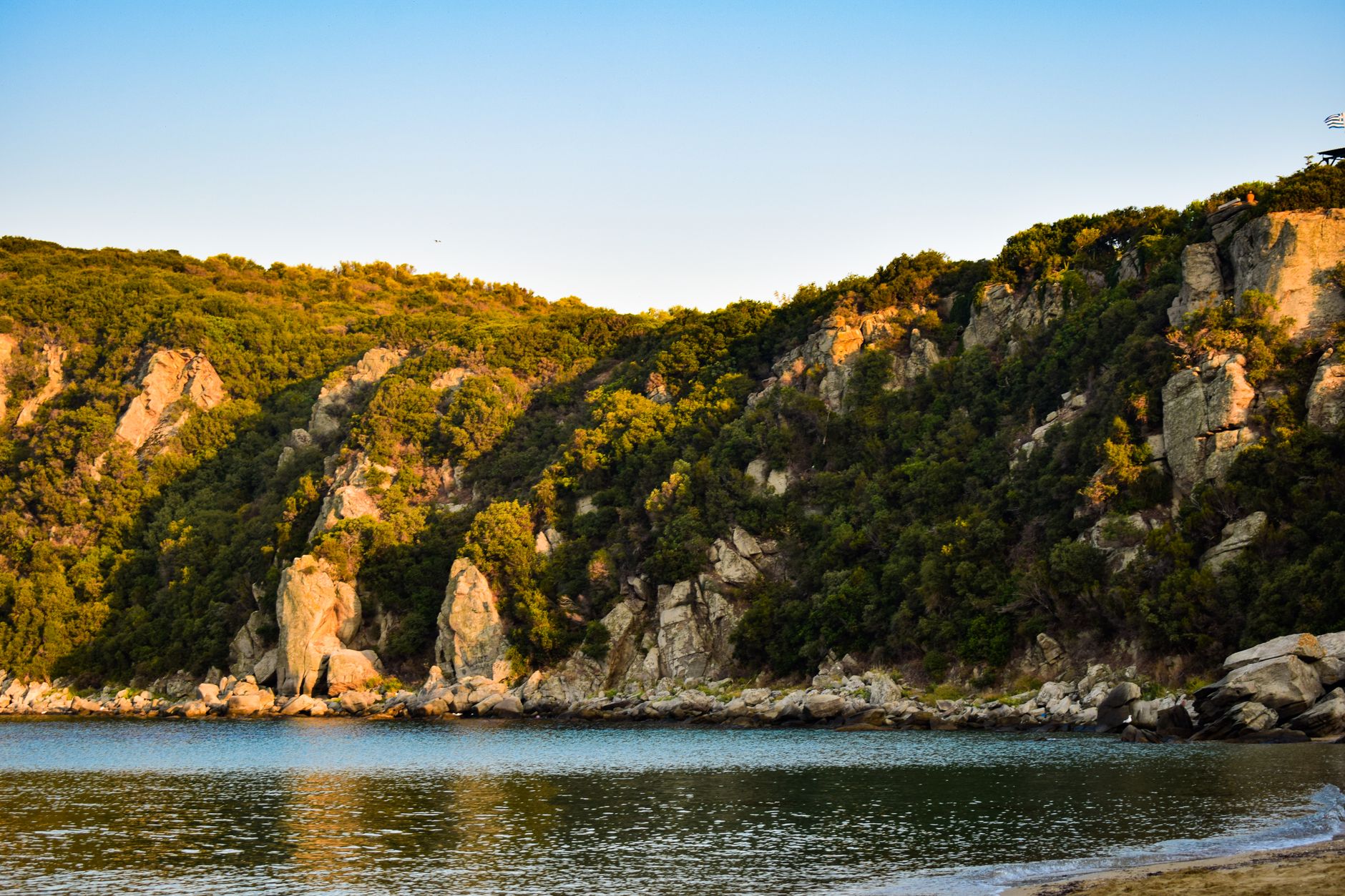 Chalkidiki, Griechenland - Peaceful Greek coastal landscape with sunlit cliffs and calm blue sea under a cl