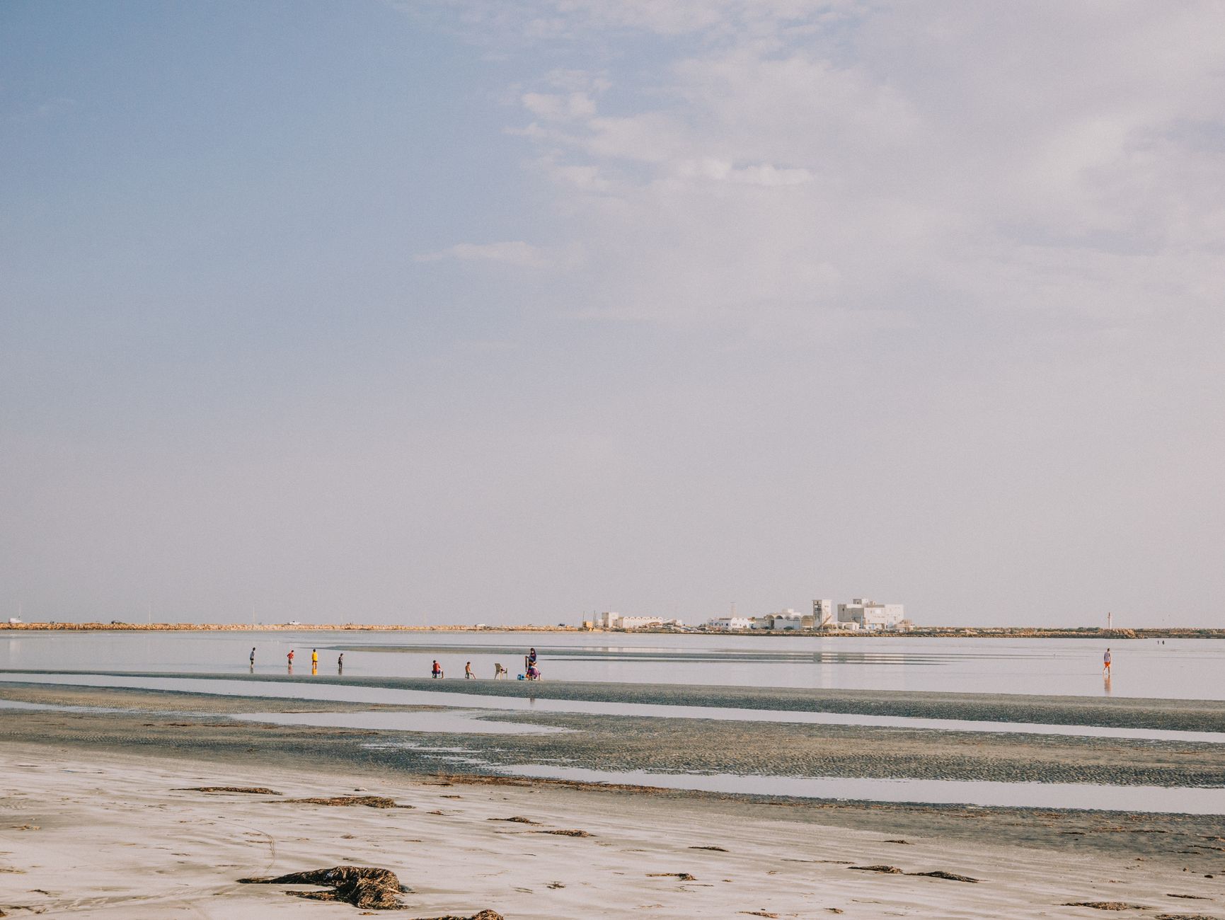 Djerba, Tunesien - Tranquil beach landscape with people walking along the shore under a clear sky.