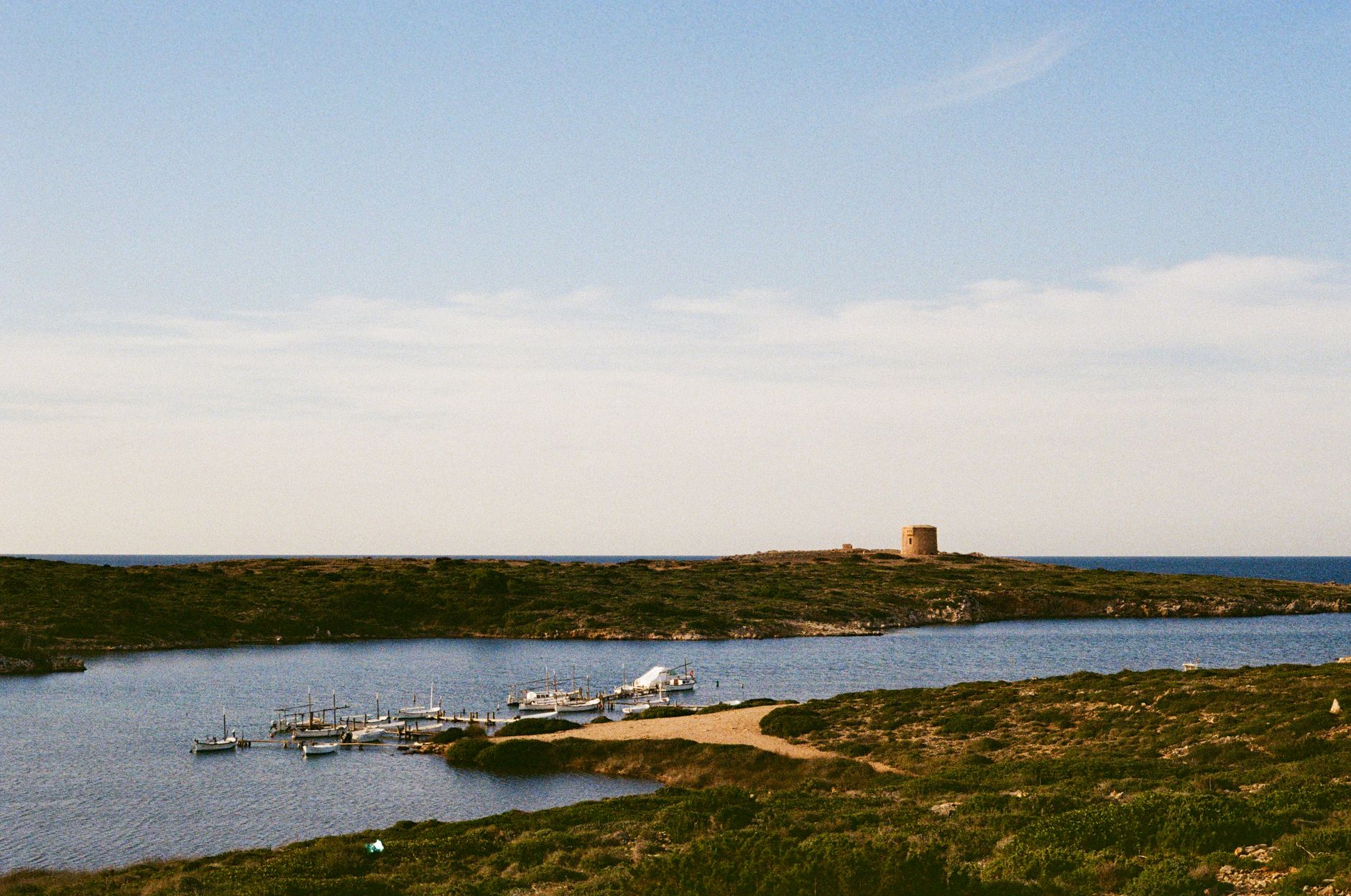 Formentera - Tranquil coastline with boats docked and a historic tower in view.