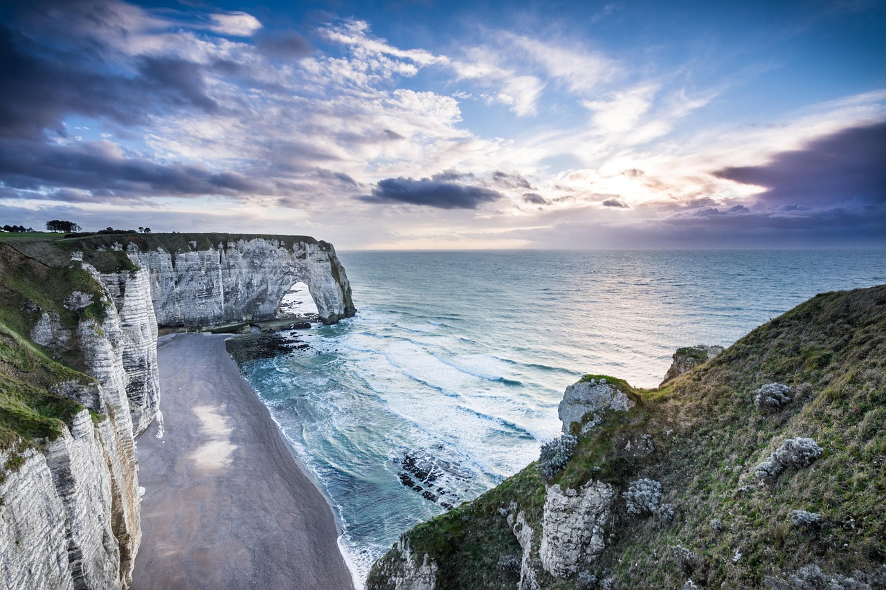 Die Kreidefelsen von Etretat mit einem natürlichen Felsenbogen, der ins Meer ragt, und einem Kiesstrand.