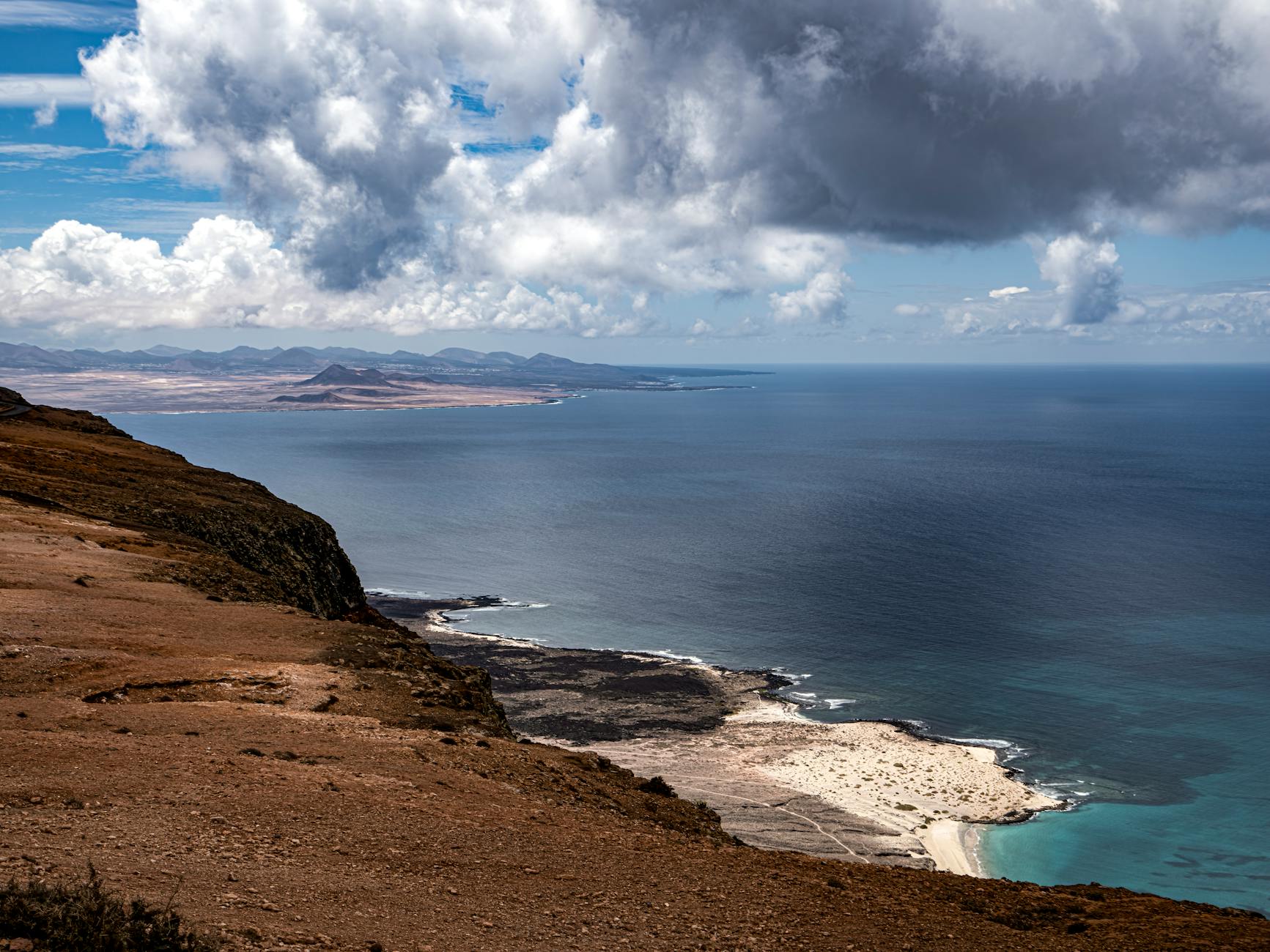 Blick von einer felsigen Klippe auf eine Kuestenlandschaft mit dem Meer und einer Insel in der Ferne.