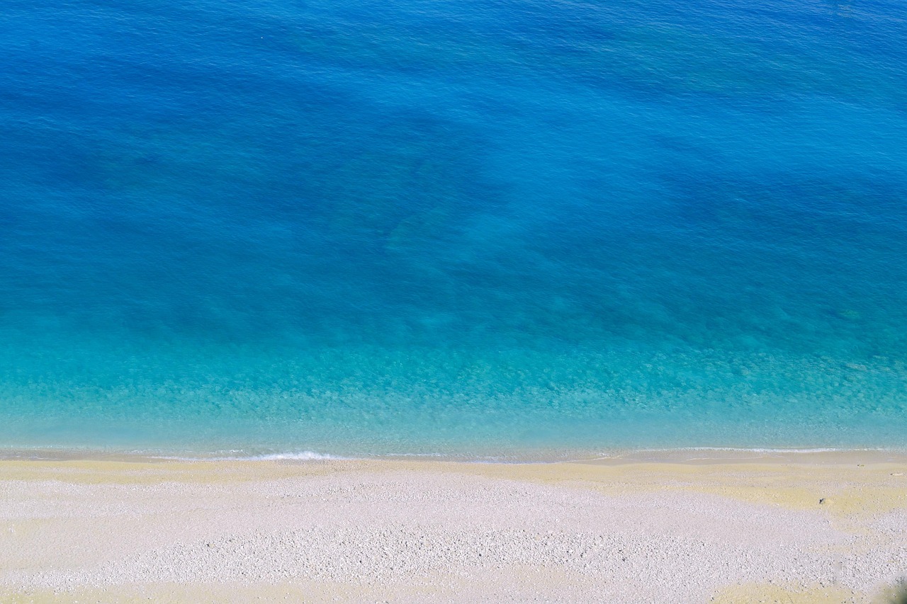 Luftaufnahme eines Kiesstrandes, der in das klare, tuerkise und blaue Meer uebergeht.