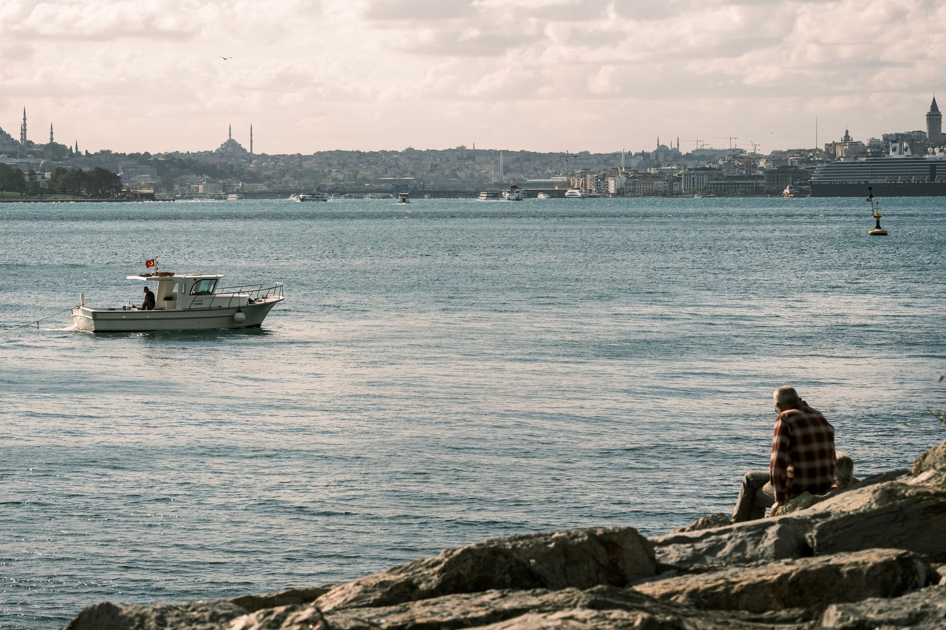 Istanbul, Türkei - Serene view of a boat and a fisherman by the Bosphorus in İstanbul, Türkiye, wit