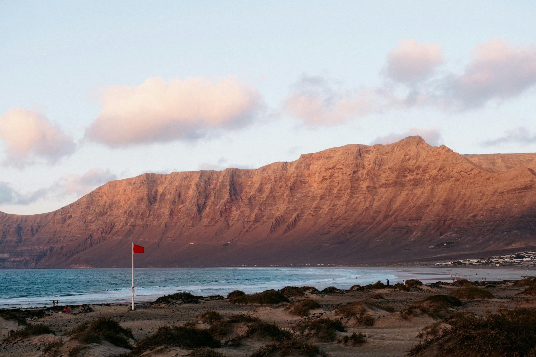 Kanaren, Spanien - Ein roter Flagge steht am Strand vor einer bergigen Küstenlinie und dem Meer.