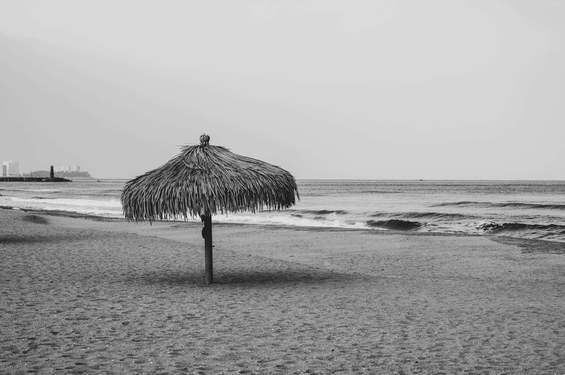 Kanaren, Spanien - Ein einzelner Strohsonnenschirm steht am Sandstrand mit dem Meer und Wellen im Hintergrund.