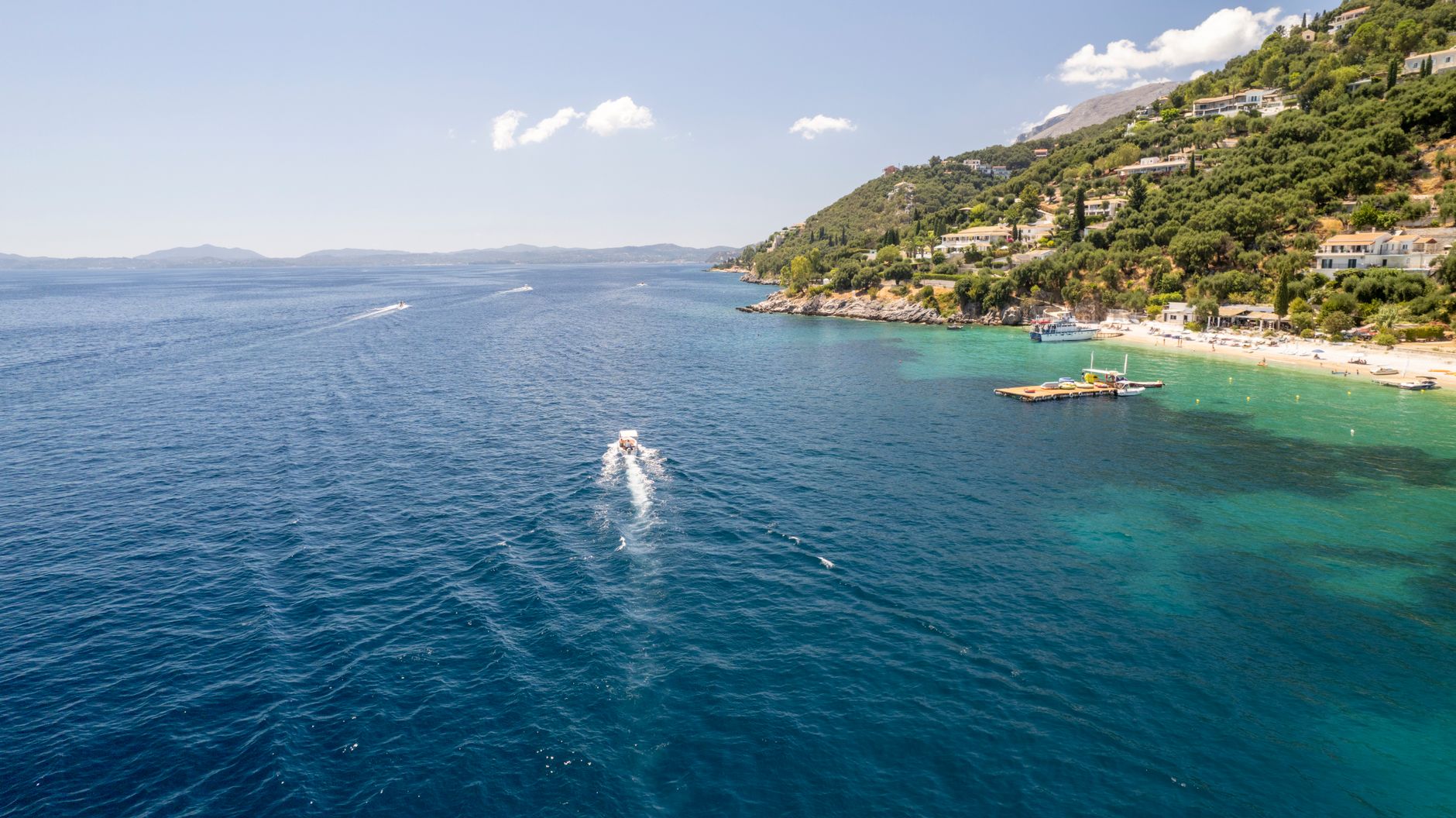 Korfu - Scenic view of Corfu's coastline featuring a boat on the blue sea under a clear 
