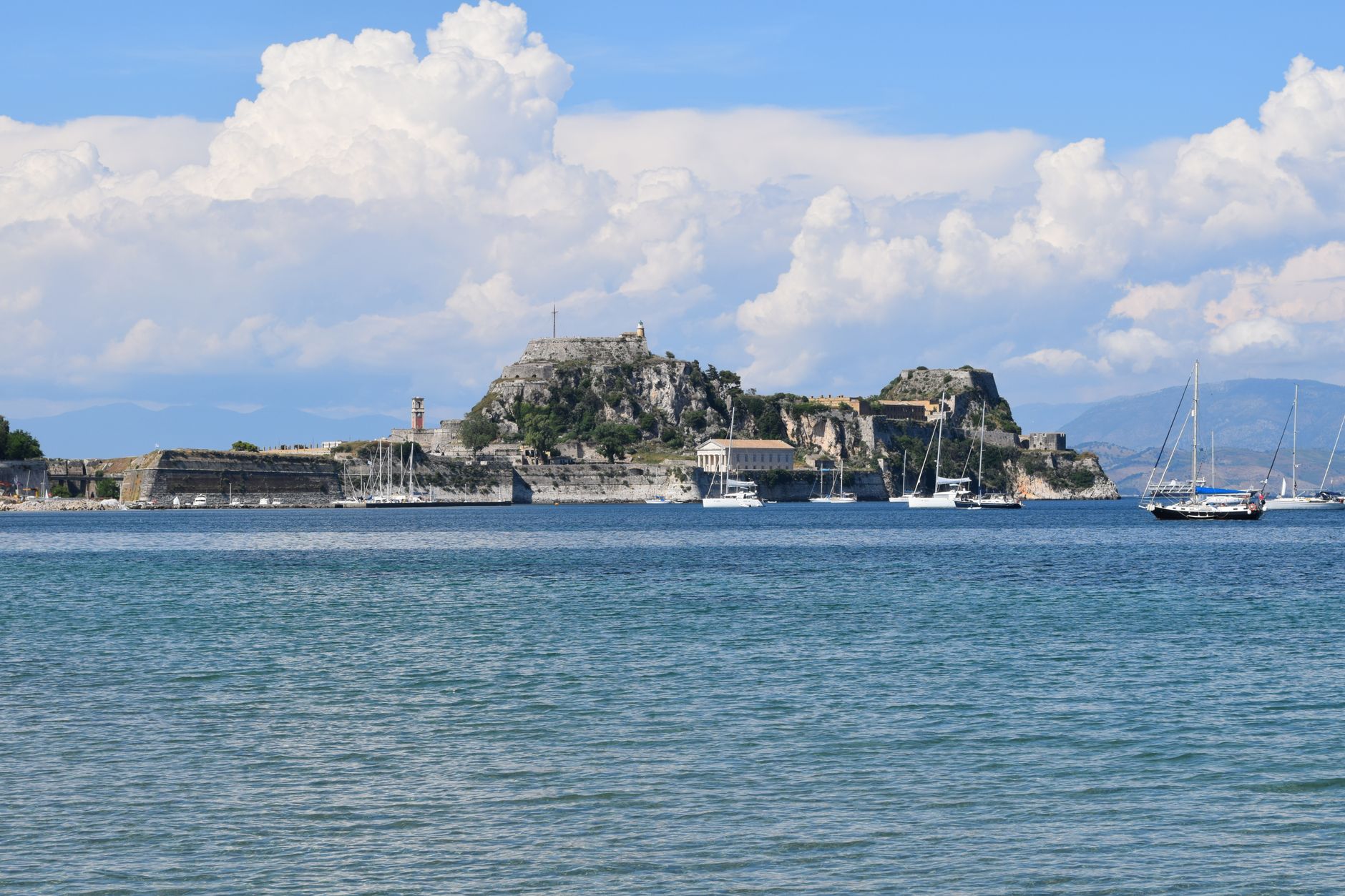 Korfu - Scenic view of Corfu's old fortress and sailboats under a blue sky.