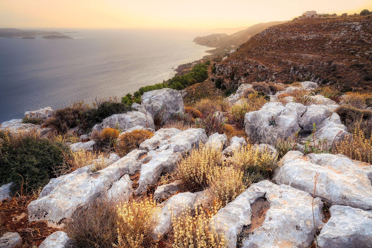Felsige Kuestenlandschaft mit mediterraner Vegetation und Blick auf das Meer bei Sonnenuntergang.