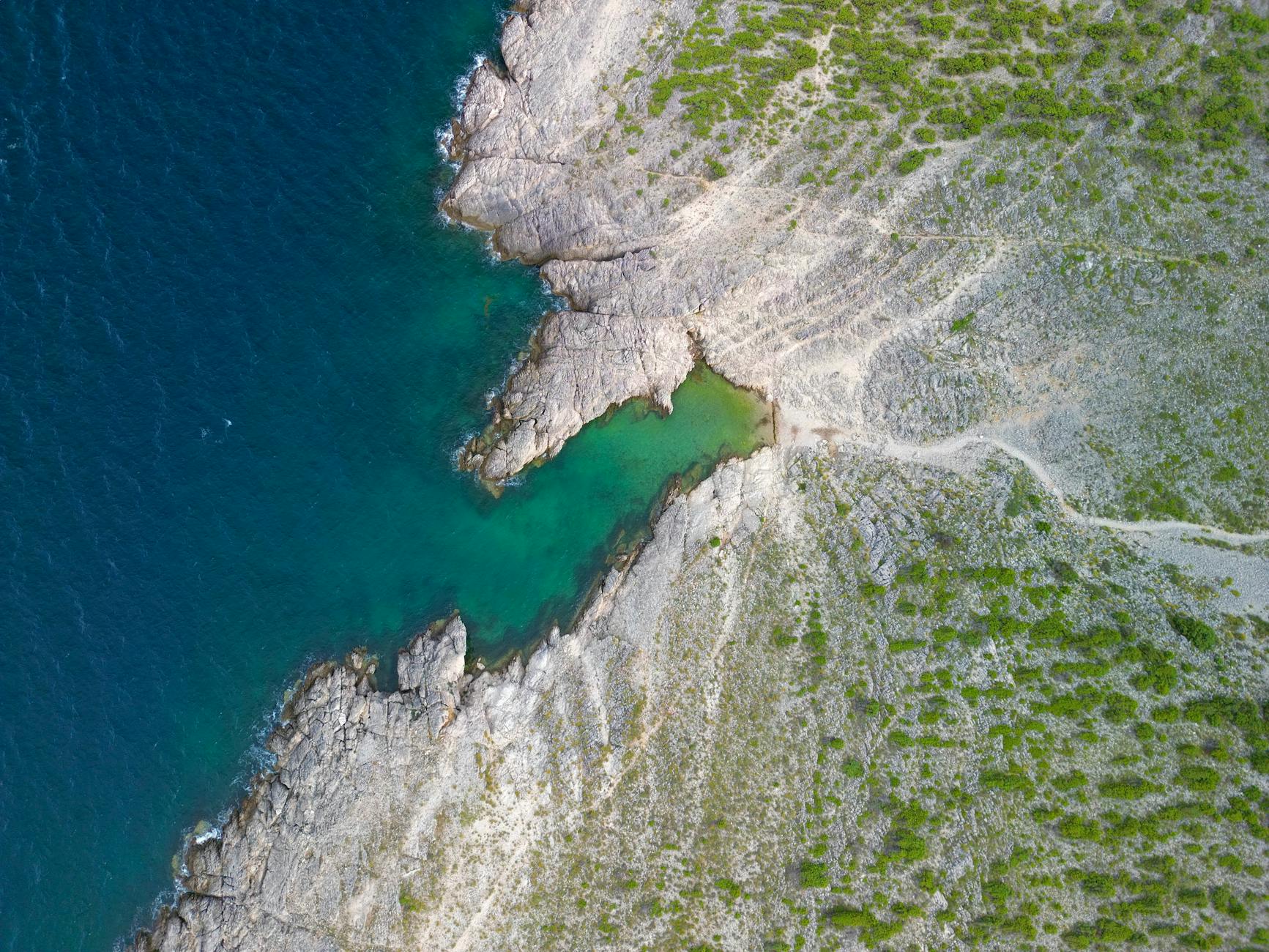 Luftaufnahme einer felsigen Küste mit türkisfarbenem Wasser und grüner Vegetation.