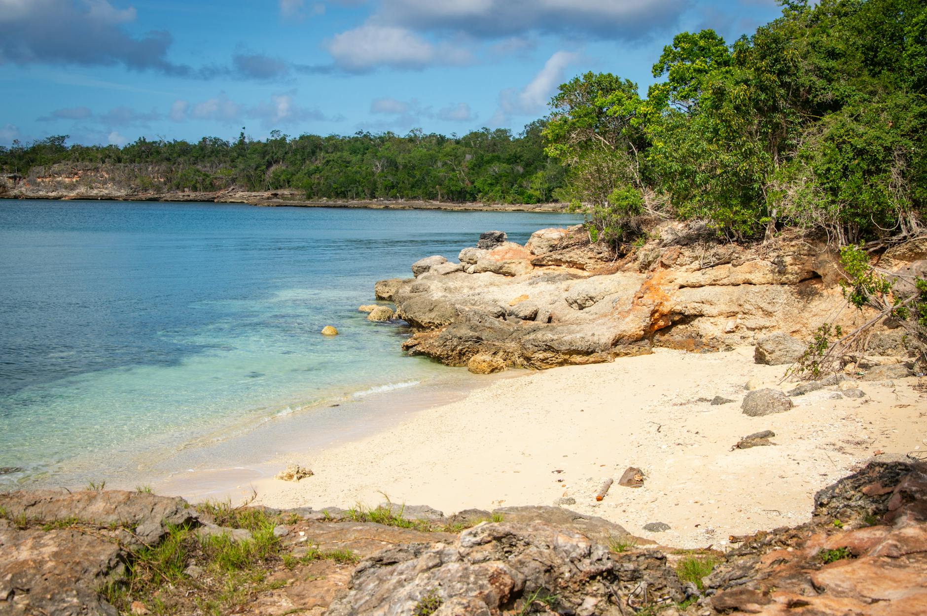 Ein kleiner Sandstrand mit felsigen Klippen und üppiger Vegetation, der in das klare, türkisfarbene Meer übergeht.
