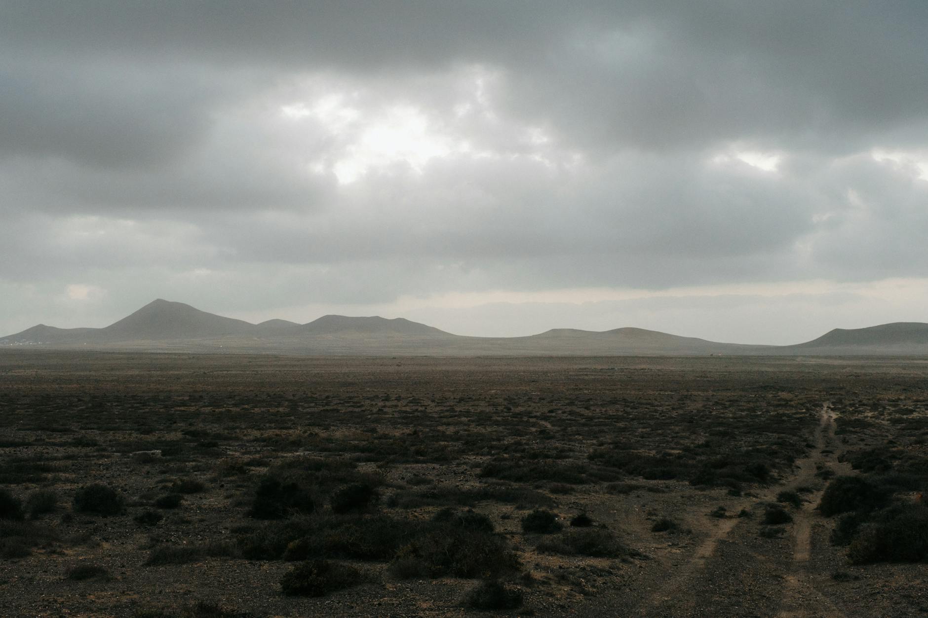 Eine weite, karge Vulkanlandschaft unter einem bedeckten Himmel mit sanften Hügeln am Horizont.