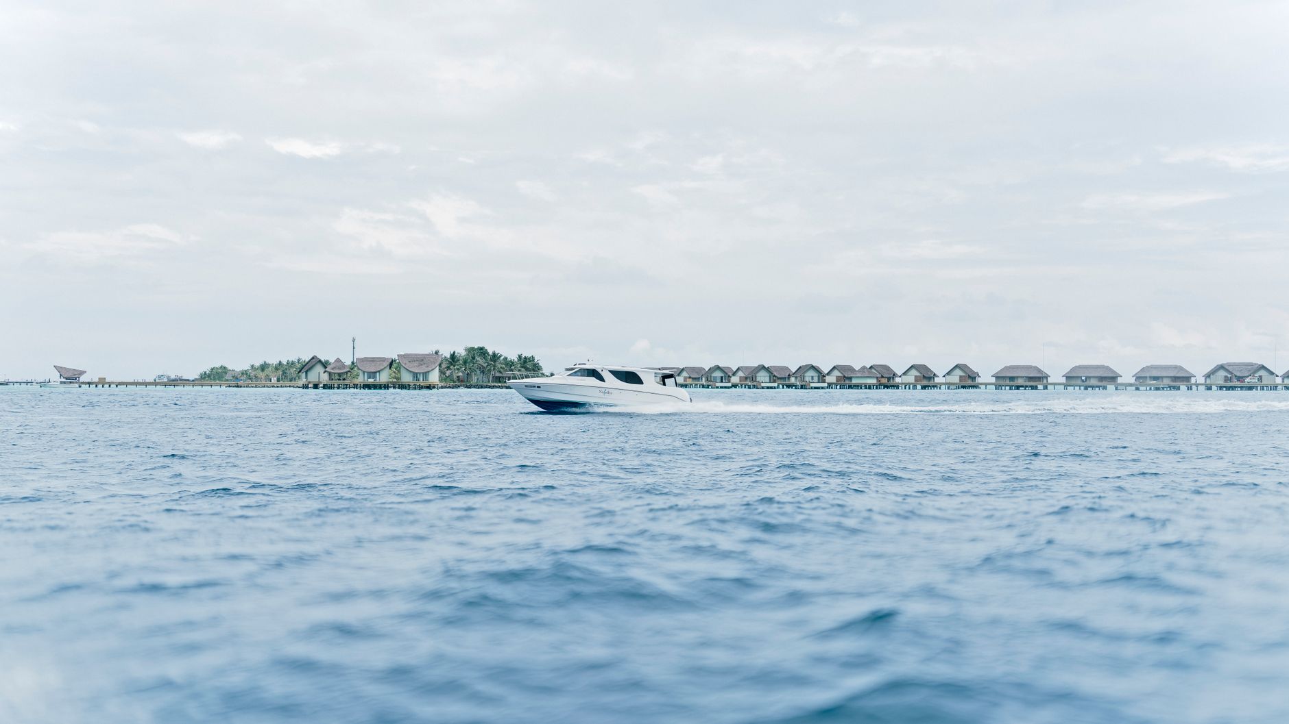 Malediven - Tranquil scene of a speedboat cruising past overwater villas in the Maldives, un