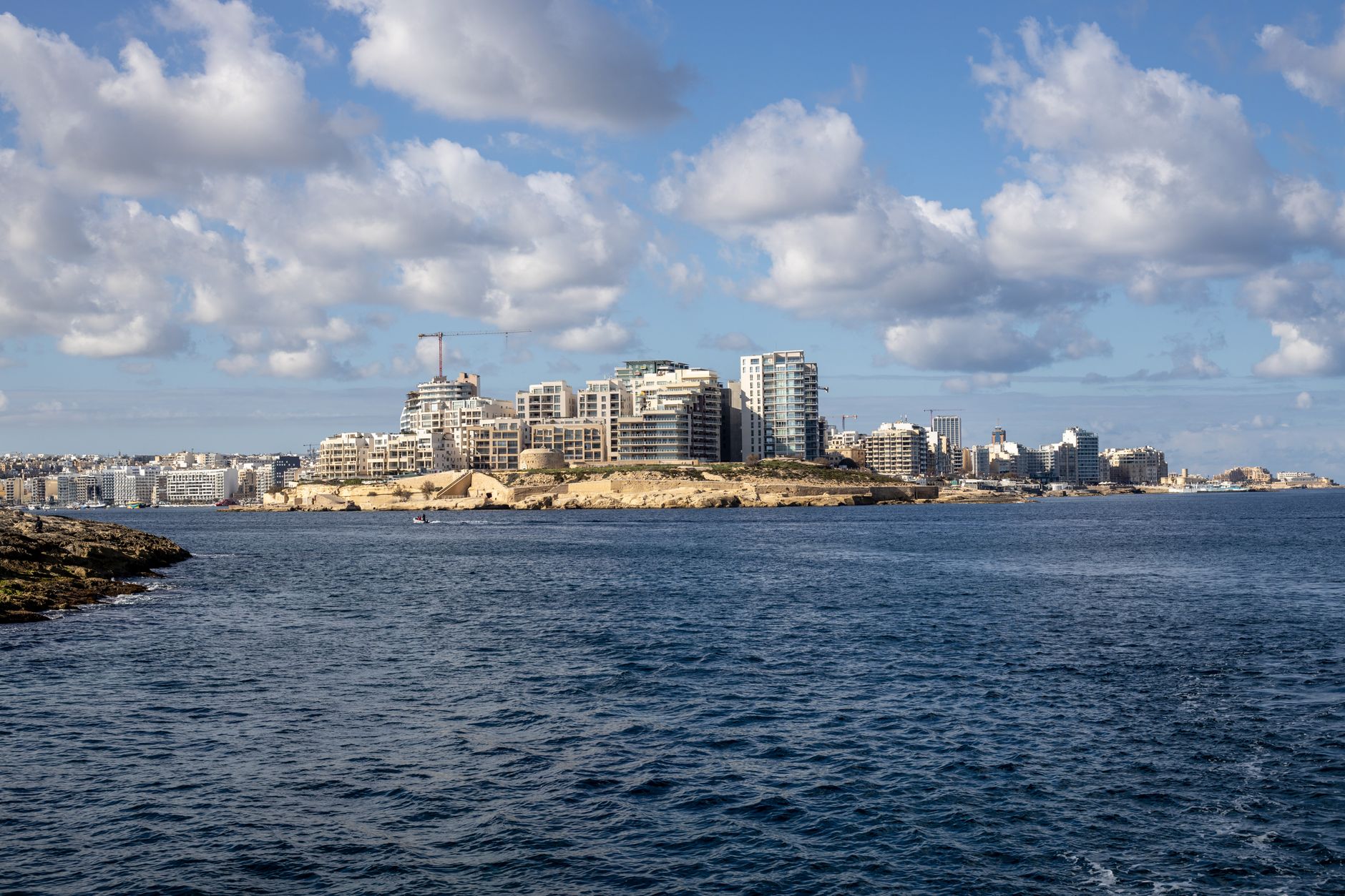 Malta - A scenic view of a coastal city skyline with blue skies and scattered clouds.