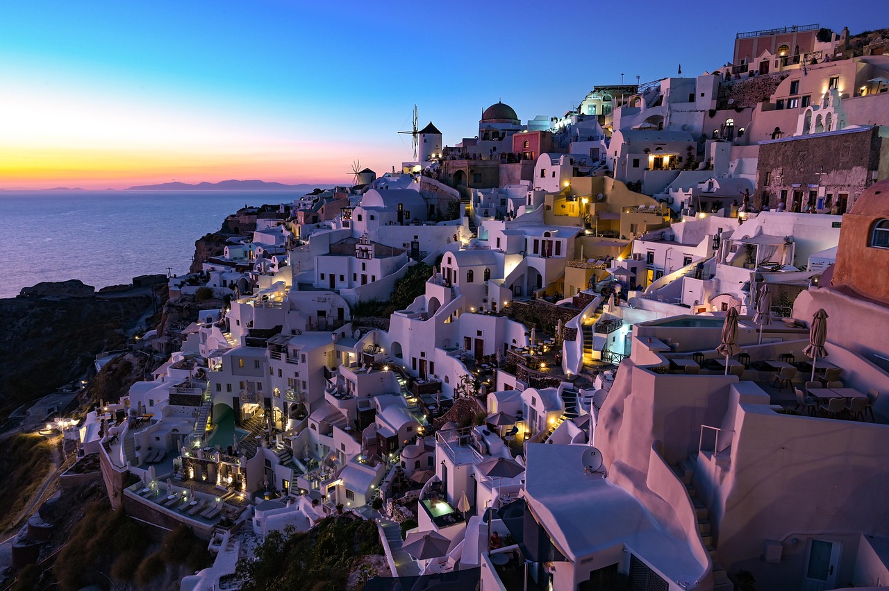 Die weissen Haeuser von Oia auf Santorini, Griechenland, schmiegen sich an einen steilen Hang ueber dem Meer, waehrend die Sonne untergeht.