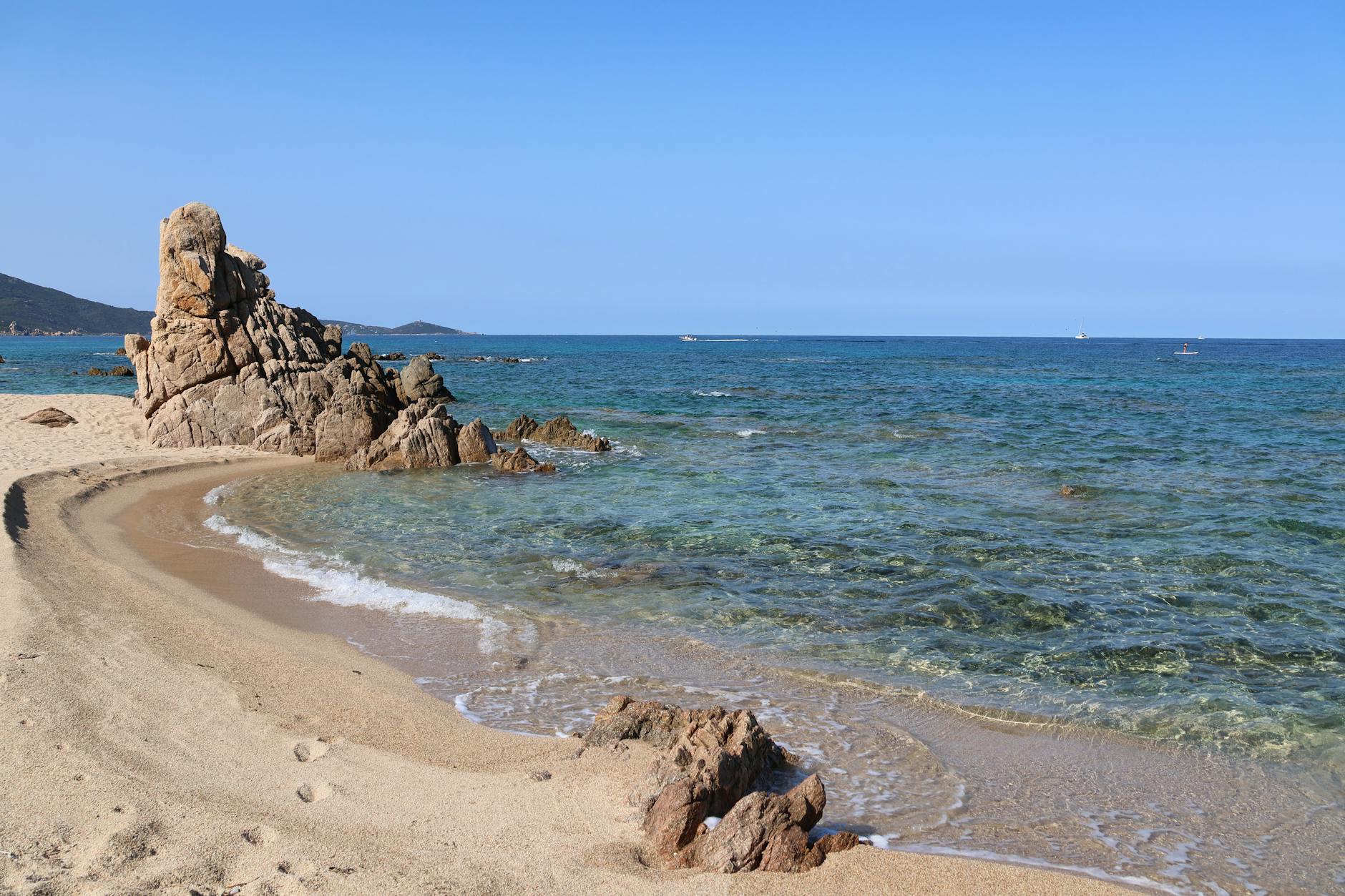 Ein felsiger Strand mit klarem, türkisfarbenem Wasser und einem sandigen Ufer unter einem strahlend blauen Himmel.