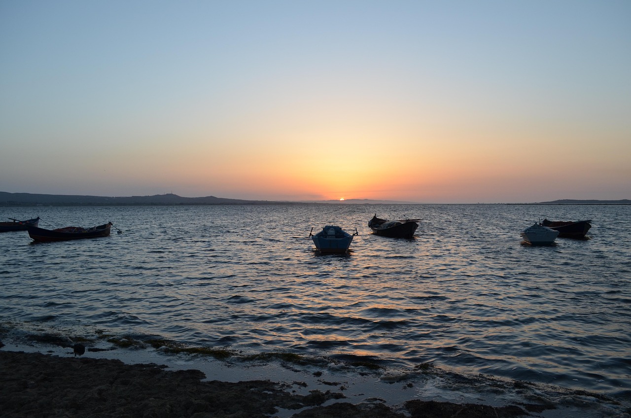 Mehrere kleine Boote treiben auf dem Meer, während die Sonne hinter dem Horizont untergeht.