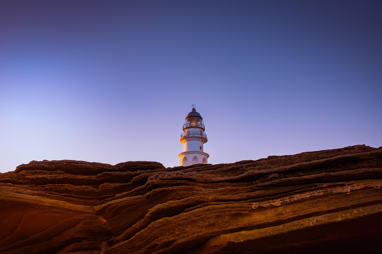 Ein weißer Leuchtturm steht auf einer felsigen Klippe im Abendlicht.