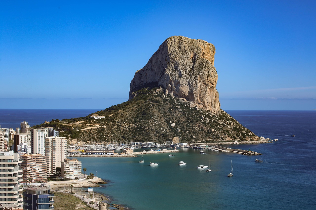 Blick auf die Stadt Calpe mit dem markanten Felsen Penon de Ifach im Hintergrund und einem Hafen mit Booten im Vordergrund.