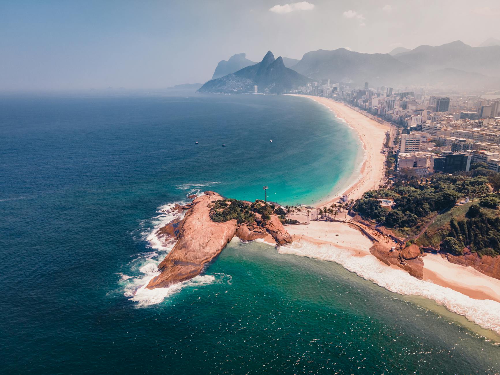 Luftaufnahme der Ipanema-Bucht in Rio de Janeiro mit dem Stadtzentrum, dem Strand und den Bergen im Hintergrund.