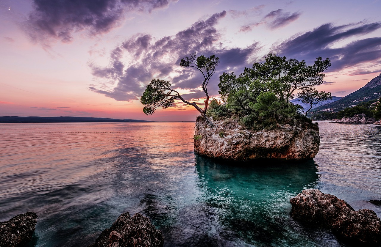 Eine felsige Insel mit Bäumen im Meer bei Sonnenuntergang.