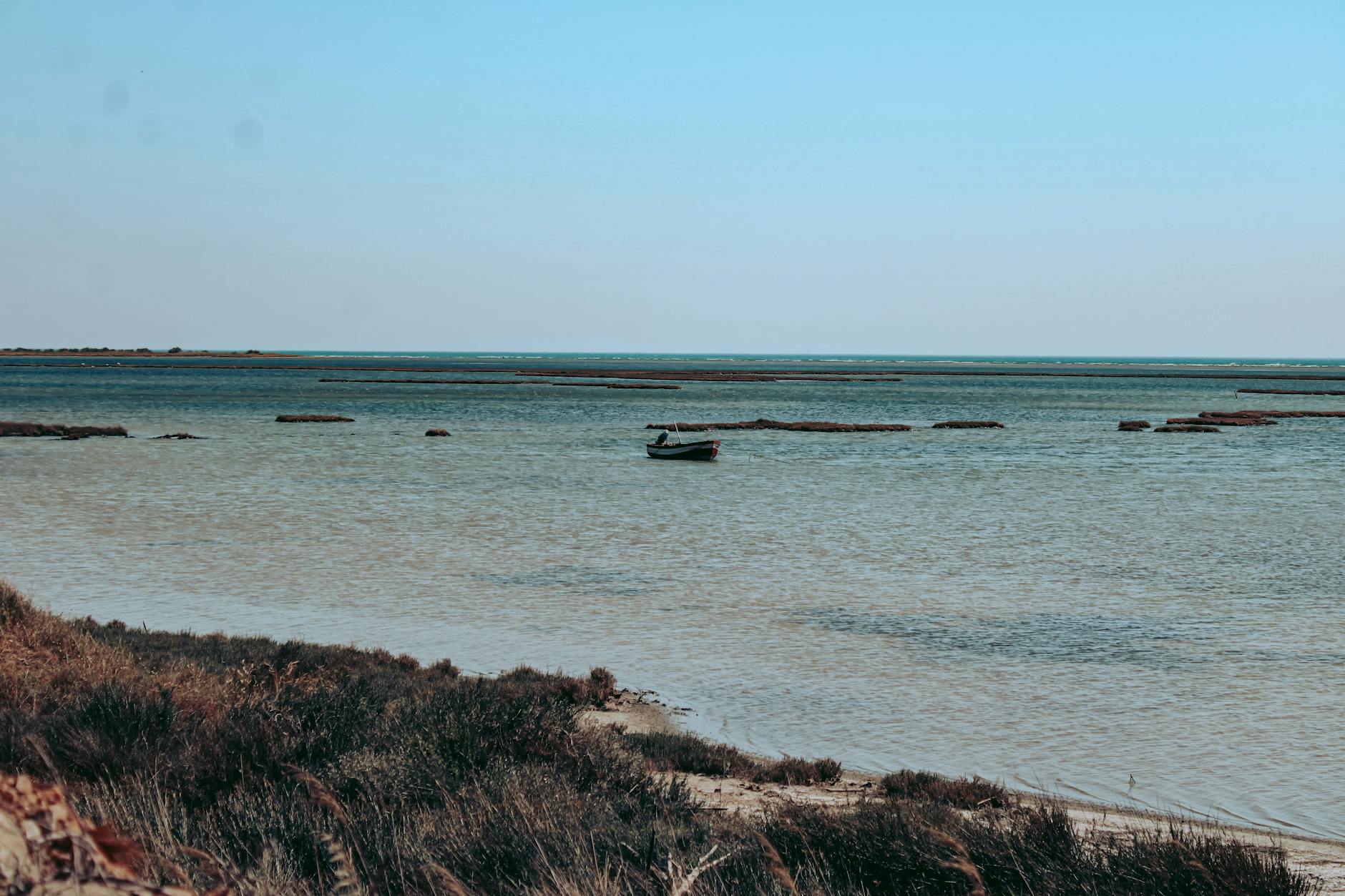 Ein kleines Boot liegt auf dem ruhigen Wasser vor einer grasbewachsenen Küste unter einem klaren Himmel.