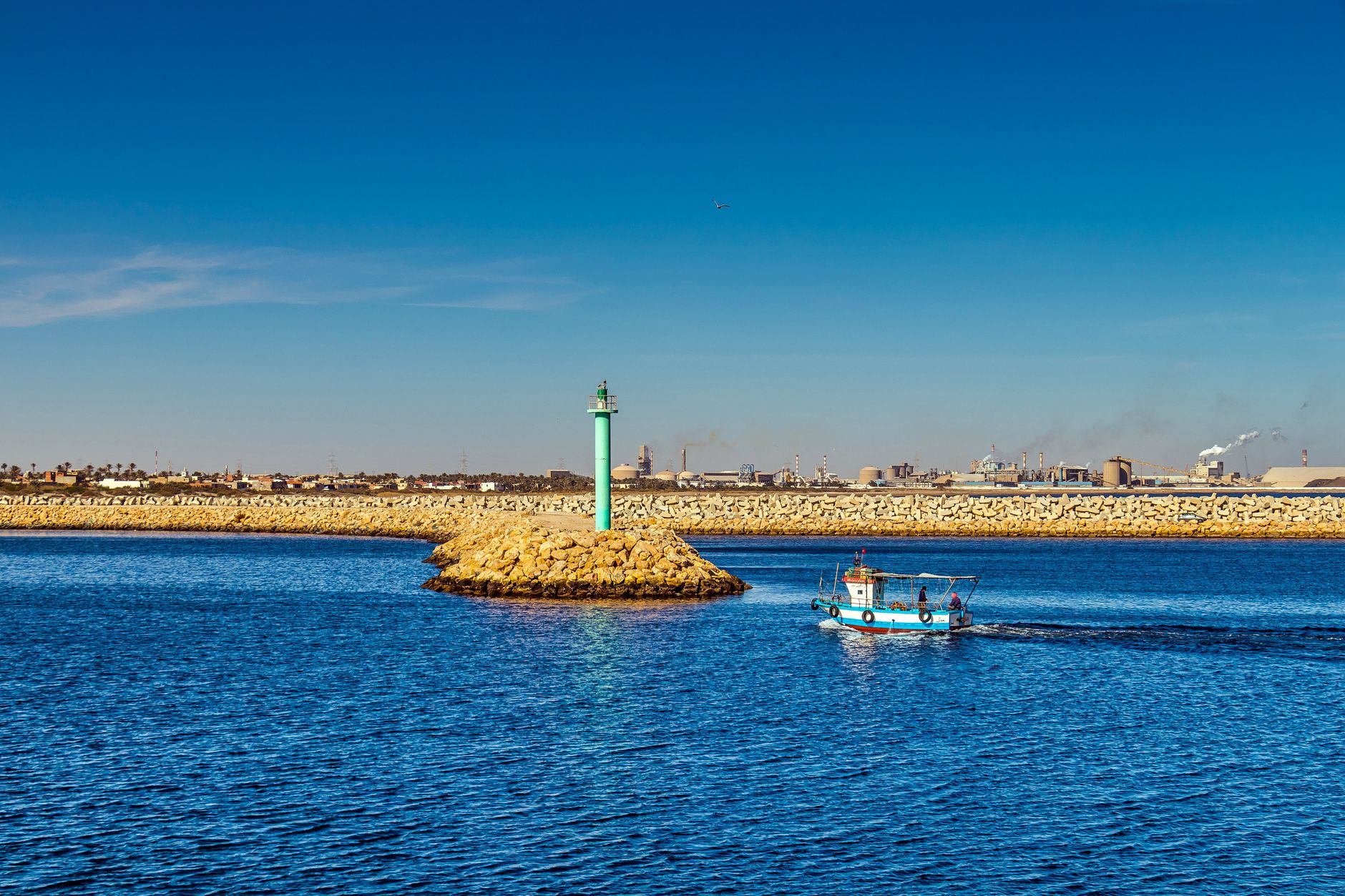 Tunesien - A small fishing boat sailing past a tall lighthouse in Gabès harbor, Tunisie.
