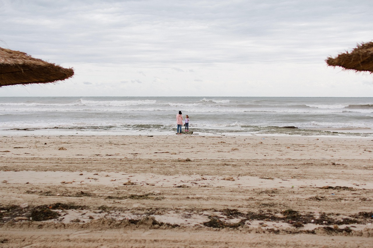Zwei Personen stehen am Strand und blicken auf das Meer, im Vordergrund sind Strandhauben zu sehen.