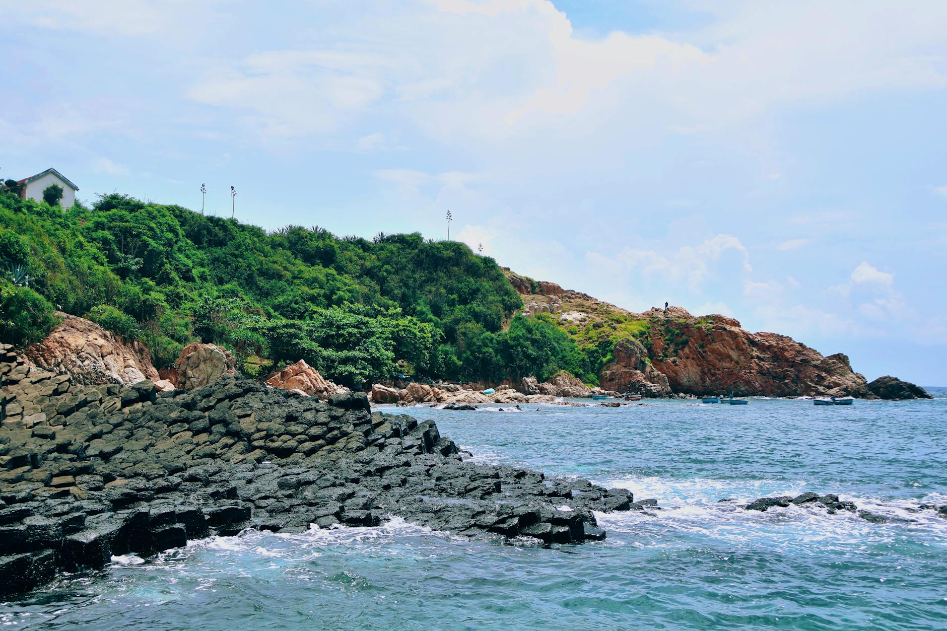 Eine felsige Kueste mit gruener Vegetation und dem blauen Meer im Vordergrund.