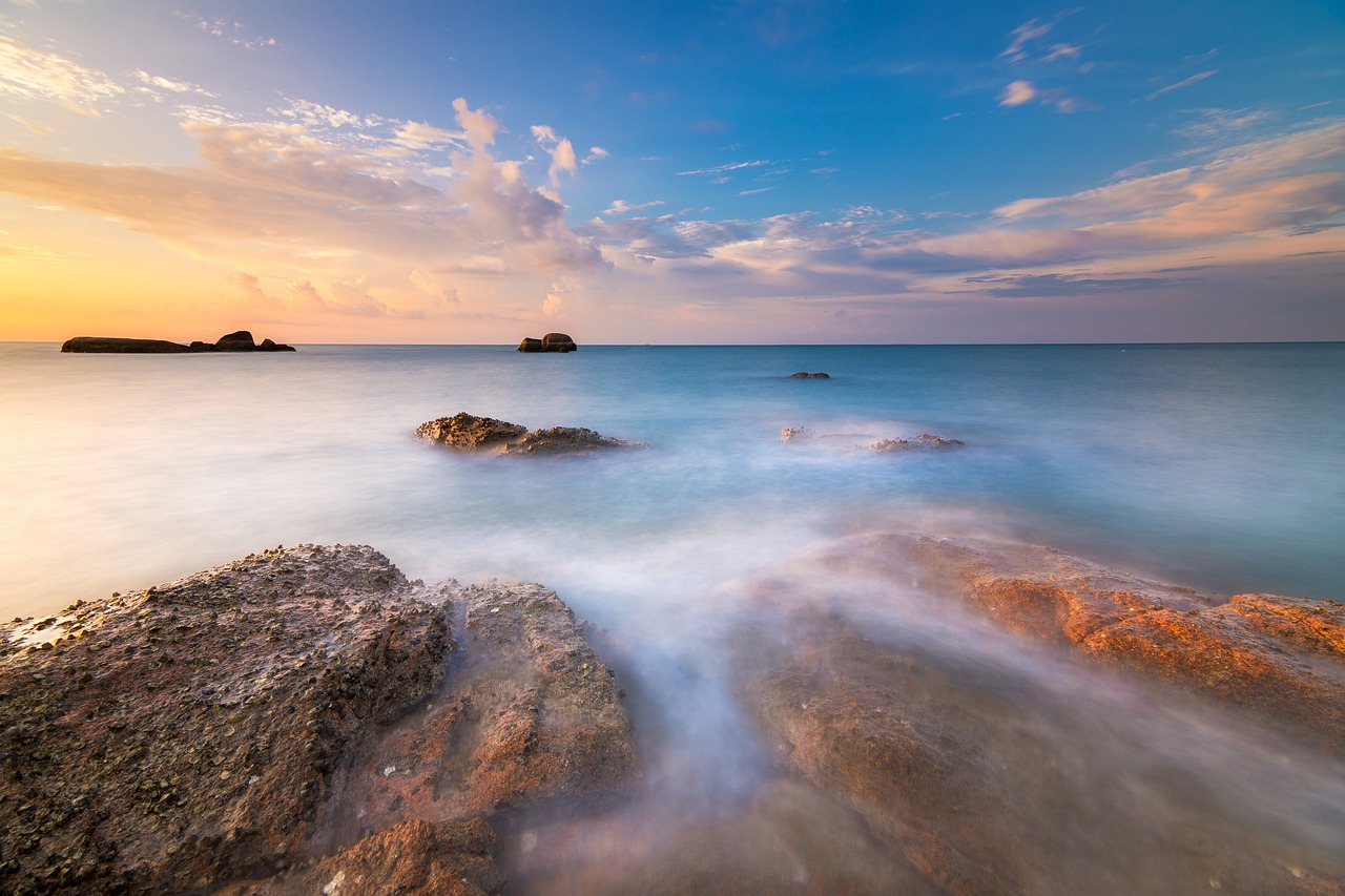 Felsen im Meer bei Sonnenuntergang mit sanften Wellen und Wolken am Himmel.