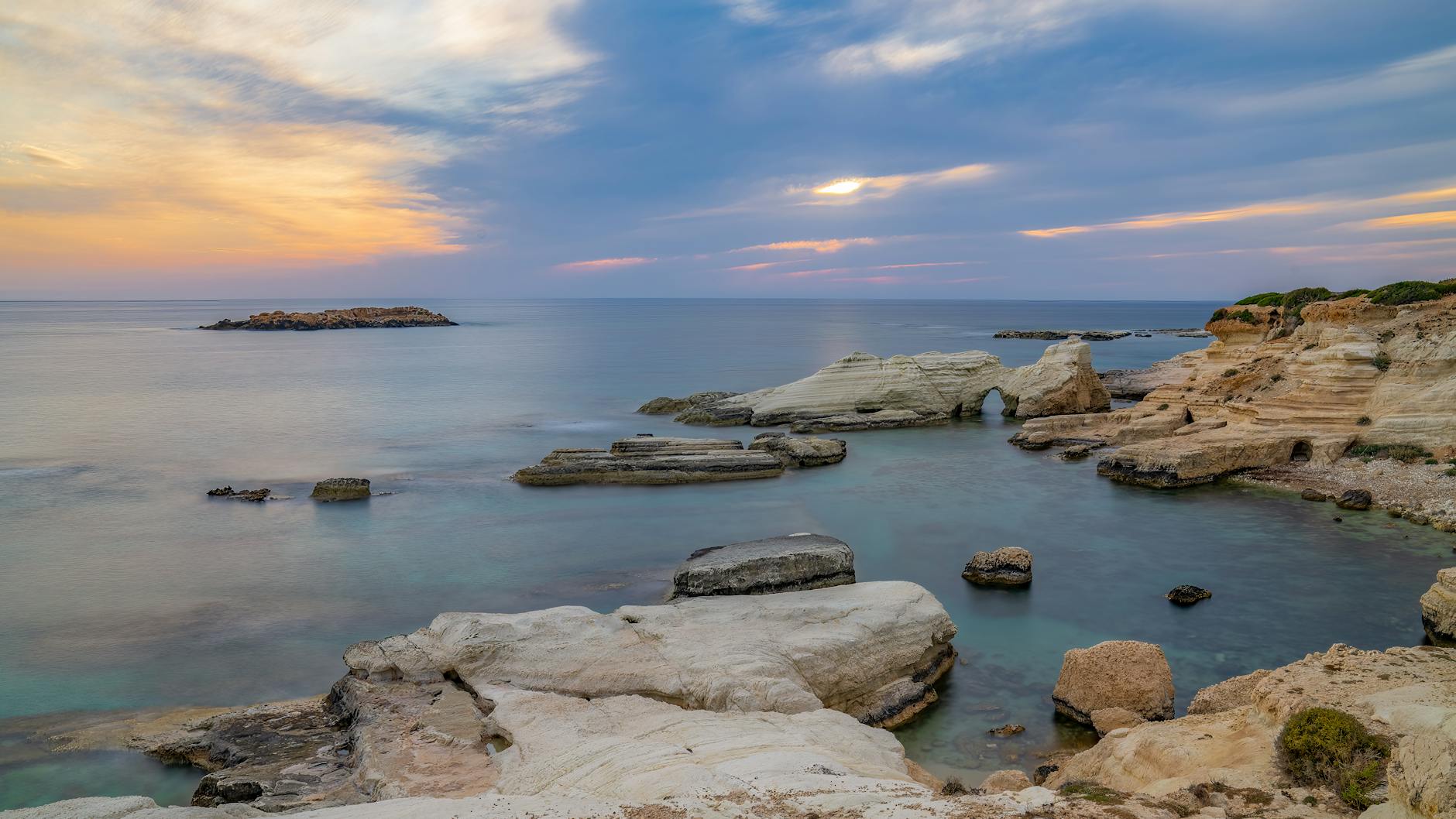Eine felsige Kueste mit einem natuerlichen Felsbogen im Meer waehrend des Sonnenuntergangs.