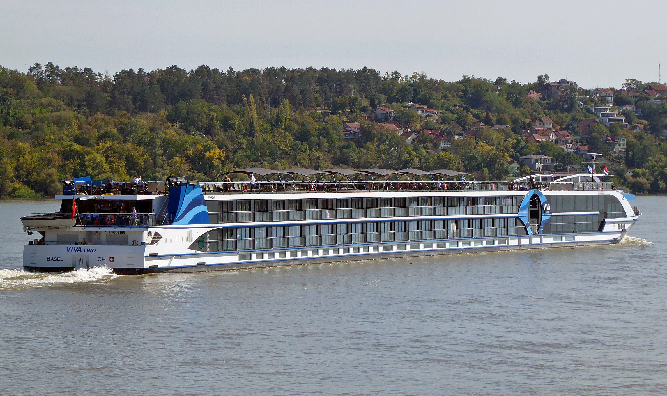 Ein Flusskreuzfahrtschiff mit dem Namen VIVA TWO fährt auf einem Fluss, im Hintergrund eine bewaldete Hügelkette mit Häusern.